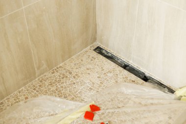 Duş gideri yerde ve modern travertin fayans mozaiği bitmemiş banyoda. Ev ve ev yenileme konsepti. Tesisat boru hatları