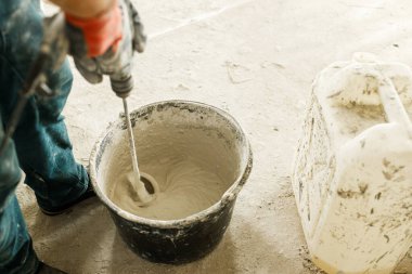 İşçi alçıtaşı alçıpan ile duvarları sıvamak için suyu karıştırıyor. Ev ve ev yenileme konsepti. Kovayı sıva karışımı ve becerikli ellerle kapat.