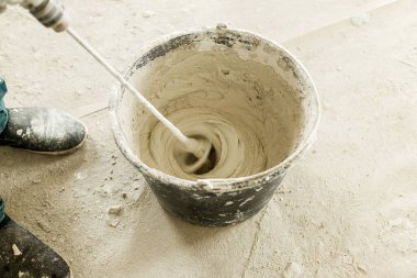 İşçi alçıtaşı alçıpan ile duvarları sıvamak için suyu karıştırıyor. Ev ve ev yenileme konsepti. Kovayı sıva karışımı ve becerikli ellerle kapat.