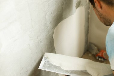 Tamirci duvarları alçıtaşı alçı ve malayla kaplıyor. Ev ve ev yenileme konsepti. İşçi ellerini spatula ve sıva ile kapatın.