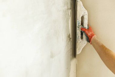 Tamirci duvarları alçıtaşı alçı ve malayla kaplıyor. Ev ve ev yenileme konsepti. İşçi ellerini spatula ve sıva ile kapatın.