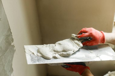 Tamirci duvarları alçıtaşı alçı ve malayla kaplıyor. Ev ve ev yenileme konsepti. İşçi ellerini spatula ve sıva ile kapatın.