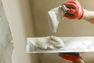 Tamirci duvarları alçıtaşı alçı ve malayla kaplıyor. Ev ve ev yenileme konsepti. İşçi ellerini spatula ve sıva ile kapatın.