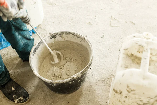 stock image Worker mixing gypsum plaster with water for plastering walls. Construction of house and home renovation concept. Close up of bucket with putty mix and handyman hands