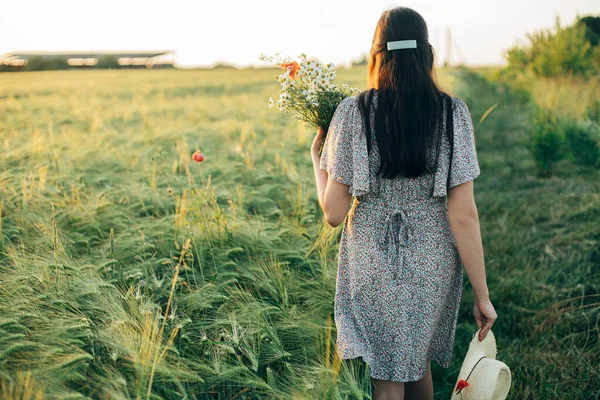 美丽的女人 戴着野花和草帽 在夕阳西下行走在大麦地里 时尚的女性在夏夜的乡间放松 大气宁静的时刻 — 图库照片