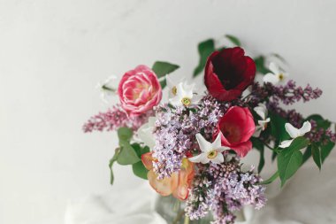 Anneler Günün kutlu olsun. İlkbahar leylağı, laleler, nergisler modern kırsal odada yumuşak kumaş üzerine düzenlenir. Kırsal ahşap masada şık bir buket. Mutlu Kadın Günleri