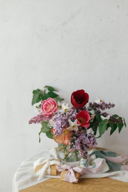 Kırsal ahşap masa üzerinde hediye kutusu olan şık bir buket. Anneler Günün kutlu olsun. Bahar leylağı, laleler, nergisler modern kırsal odadaki yumuşak kumaşlarda mevcut. Mutlu Kadın Günleri