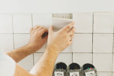 Eller yapıştırıcıya modern kare fayanslar seriyor. İşçi, alçı duvara şık beyaz fayanslar yerleştiriyor. Yenileme