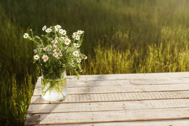 Güzel kır çiçekleri, güneş ışığında otların arkasındaki ahşap masa üzerinde. Bahçeden toplanan vazodaki güzel yaz çiçekleri, kırsal evdeki düzenlemeler. Boşluğu kopyala