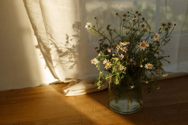 stock image Stylish wildflowers bouquet in evening sunlight against window in rustic room. Beautiful summer flowers in vase gathered from garden, floral arrangement in countryside home