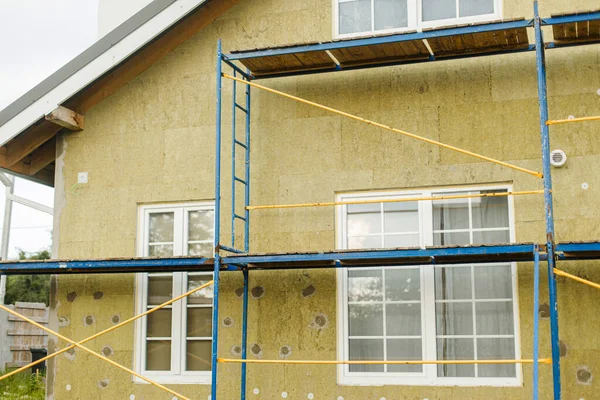 House insulation concept. Facade insulation with mineral wool, thermal improvement and energy saving. Modern farmhouse renovation, scaffolding platform and stone wool panels