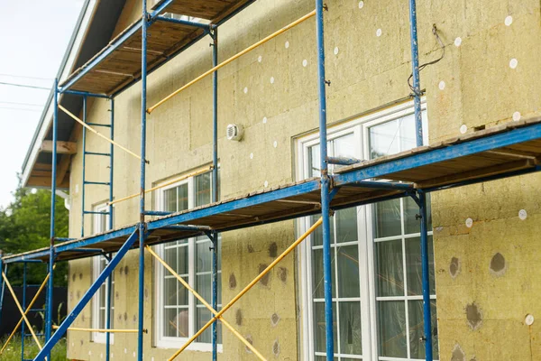 Facade insulation with mineral wool, thermal improvement and energy saving. Modern farmhouse renovation, scaffolding platform and stone wool panels. House insulation concept