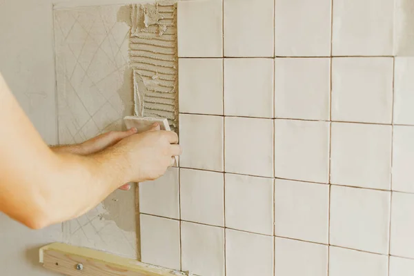 在阳光下的灰泥墙上安装时尚的白色瓷砖的工人 手把现代正方形的瓷砖贴在胶粘剂上 厨房或浴室翻新 住房装修 — 图库照片