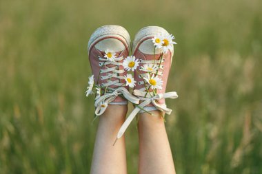 Yaz kırsalında papatya çiçekli pembe spor ayakkabılı kadın bacakları, yakın çekim. Genç bir dişi çayırda kır çiçeklerinin arasında dinleniyor. Tasasız ve yaz tatili, komik bir an.