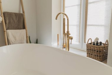 Şık bir banyo tasarımı. Zeminden altın musluğu olan modern küvet, havluklu ahşap merdiven, temel çamaşır malzemeleri ve büyük pencere, modern ekolojik banyo iç mimarisi..