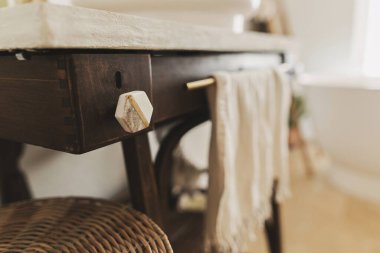 Modern mermer kulplu, taşralı ahşap tezgahın üzerinde küvetin arka planında havlu, boho banyo tasarımı ayrıntıları. Banyo içi çok şık.