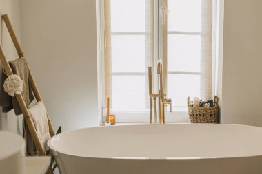 Şık bir banyo tasarımı. Zeminden altın musluğu olan modern küvet, havluklu ahşap merdiven, temel çamaşır malzemeleri ve büyük pencere, modern ekolojik banyo iç mimarisi..