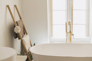 Banyo içi çok şık. Zeminden altın musluğu olan modern küvet, havluklu ahşap merdiven ve büyük pencere, boho banyo tasarımı..