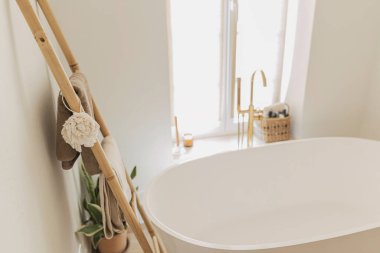 Banyo içi çok şık. Zeminden altın musluğu olan modern küvet, havluklu ahşap merdiven ve büyük pencere, boho banyo tasarımı..