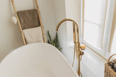 Banyo içi çok şık. Zeminden altın musluğu olan modern küvet, havluklu ahşap merdiven ve büyük pencere, boho banyo tasarımı..