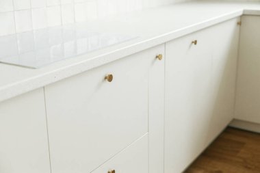 Modern mutfak iç mimarisi. Pirinç düğmeli şık beyaz mutfak dolapları, granit tezgah ve yeni İskandinav evinde elektrikli soba. Modern mutfak atölyesi