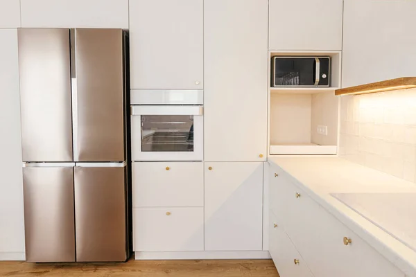 现代厨房的内部 时尚的白色厨房橱柜与黄铜把手 花岗岩柜台 木制架子与照明和器具在新的丑闻鸟屋 现代最低厨房设计 — 图库照片