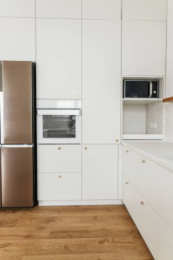 Modern mutfak tasarımı. Yeni İskandinav evinde pirinç düğmeleri, ahşap rafları ve aletleri olan şık beyaz mutfak dolapları. Modern mutfak iç mimarisi