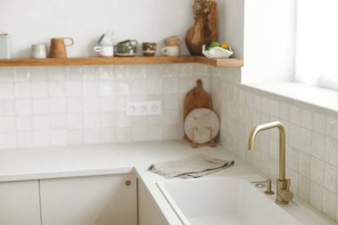 Şık beyaz mutfak dolapları, pirinç musluk ve granit lavabo, yeni İskandinav evinde çatal bıçaklı ahşap raflar. Modern mutfak tasarımı. Modern mutfak iç mimarisi