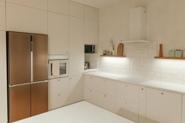Modern mutfak iç mimarisi. Pirinç düğmeli şık beyaz mutfak dolapları, akşam lambalı ahşap raflar ve yeni İskandinav evinde aletler. Modern mutfak tasarımı