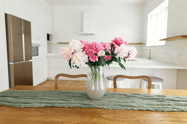 新しい家の島 木製の棚や家電製品とスタイリッシュな白いキッチンを背景に木製のテーブルの上に花瓶の美しい牡丹 農家のモダンなキッチンインテリア — ストック写真