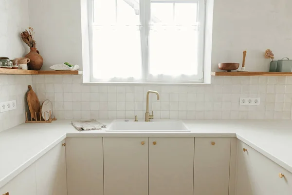 时尚的白色厨房橱柜 黄铜水龙头和花岗岩水池 新丑闻中的木制架子上的器皿 现代最小厨房设计 现代厨房内部 — 图库照片