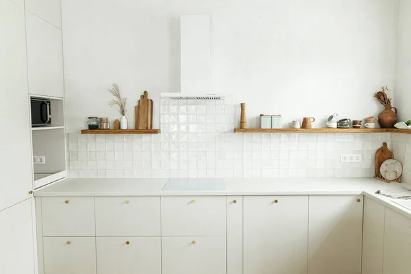 现代最小厨房设计 在新的丑闻中 风格别致的白色厨房橱柜 装有黄铜把手 花岗岩岛 木制架子上的器具和器皿 现代厨房内部 — 图库照片