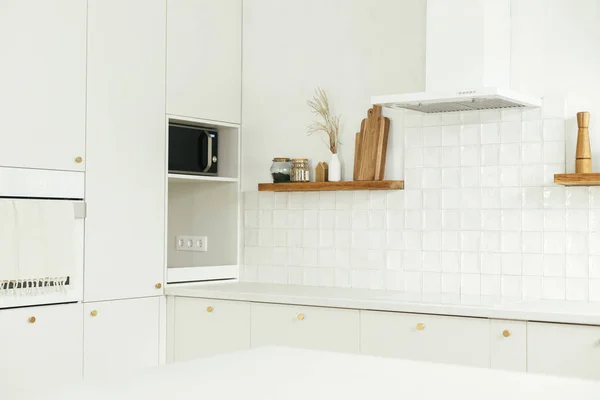 现代厨房的内部 在新的丑闻中 风格别致的白色厨房橱柜 装有黄铜把手 花岗岩岛 木制架子上的器具和器皿 现代最低厨房设计 — 图库照片