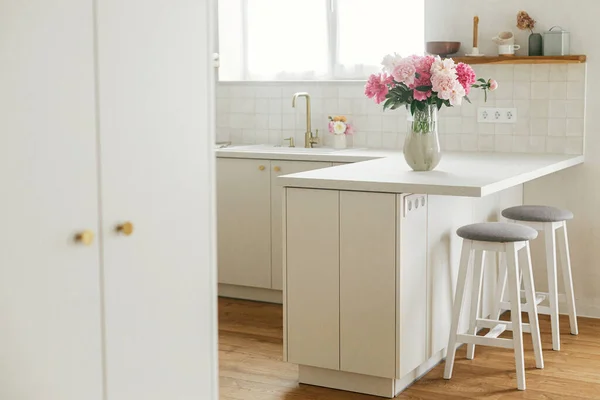 漂亮的牡丹在花岗岩台面的花瓶上 背景是时尚的白色厨房 新的房子里有木制架子和家用电器 现代最小厨房内部 — 图库照片