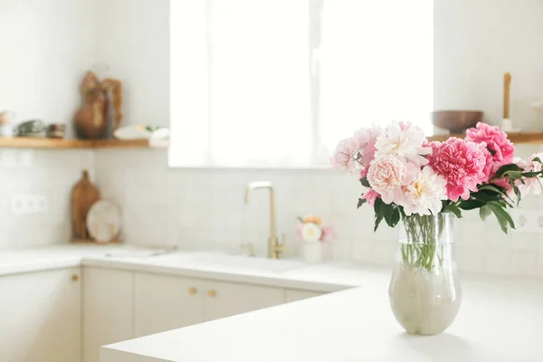 新しい家に木製の棚や家電製品とスタイリッシュな白いキッチンを背景に花崗岩のカウンターの上に花瓶の美しい牡丹 モダンなミニキッチンインテリア — ストック写真