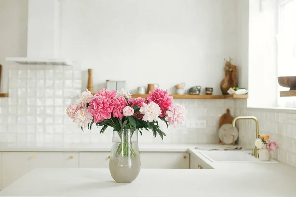 花岗岩台面花瓶上漂亮的牡丹 背景是时尚的白色厨房 新房子里有木制架子和家用电器 现代最小厨房内部 — 图库照片