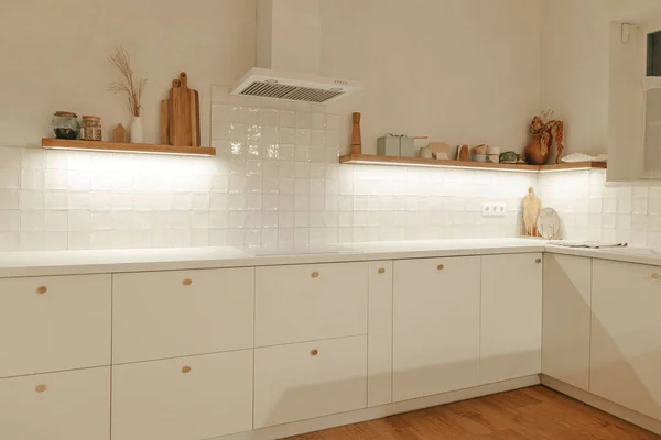 现代最小厨房设计 时尚的白色厨房橱柜 有黄铜把手 木制架子 有晚灯和新丑闻中的家用电器 现代厨房内部 — 图库照片
