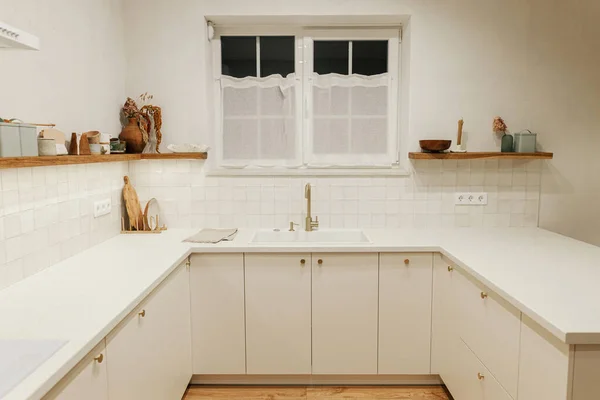 现代厨房的内部 时尚的白色厨房橱柜 黄铜水龙头和花岗岩水槽 木制架子上的器皿和夜晚的灯在新的丑闻鸟的房子 现代最低厨房设计 — 图库照片