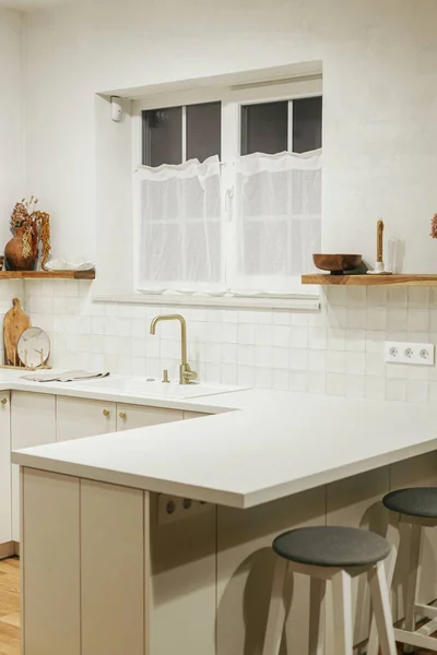 现代厨房的内部 时尚的白色厨房橱柜 黄铜水龙头和花岗岩水槽 木制架子上的器皿和夜晚的灯在新的丑闻鸟的房子 现代最低厨房设计 — 图库照片