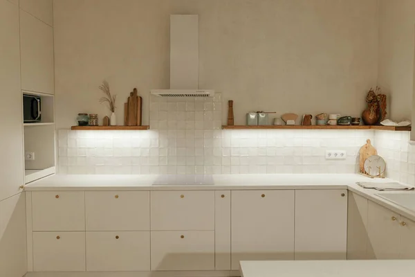 モダンなキッチンインテリア 真鍮ノブ付きのスタイリッシュな白いキッチンキャビネット 新しいスカンディナヴィアの家で夜の光と家電付きの木製の棚 モダンなミニキッチンデザイン — ストック写真