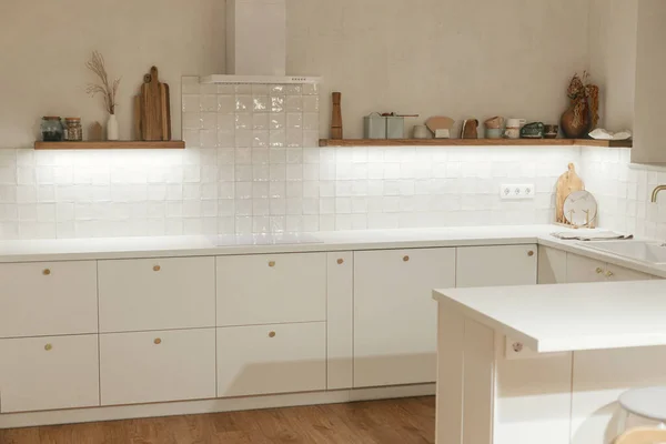现代厨房的内部 新屋的时尚白色厨房橱柜 装有黄铜把手 花岗岩岛 家用电器和夜灯 现代最低厨房设计 — 图库照片