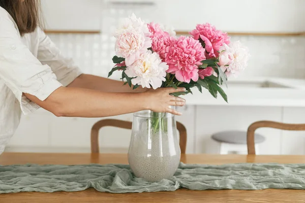 新しい現代の家の花瓶に美しい牡丹を配置する女性 小さな白いキッチンを背景に花を持つ若い女性の装飾家 花を閉じ手 — ストック写真