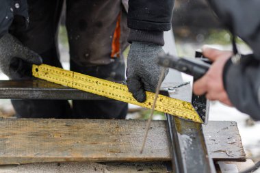 Açı cetveli işçilerin elinde, insan metali elektrotlarla kaynaştırıyor. Kalkanlı metal kaynaklama. Yay kaynaklama ve dairesel öğütücüden çit yapan işçiler için araçlar