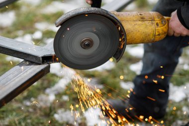 Açı öğütücü makinesiyle metal kesmek. Dairesel öğütücü diski ve elektrik kıvılcımlarını kapatın. İşçiler kalkanlı metal kaynaklarla çit yapıyorlar.