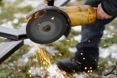Dairesel öğütücü disk ve elektrik kıvılcımlarıyla metal öğüten adama yaklaş. Kaynak yapmak için metal kesen bir işçi. İşçiler kalkanlı metal kaynaklarla çit yapıyorlar.