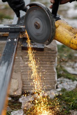 Dairesel öğütücü disk ve elektrik kıvılcımlarıyla metal öğüten adama yaklaş. Kaynak yapmak için metal kesen bir işçi. İşçiler kalkanlı metal kaynaklarla çit yapıyorlar.