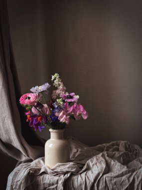 Kasvetli kırsal arka planda vazodaki güzel çiçekler. Şık çiçekler natürmort, latilus, anemon, ranunculus, dezenyum gibi sanatsal bileşimler. Çiçek dikey duvar kağıdı