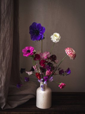 Kasvetli kırsal arka planda vazodaki güzel çiçekler. Şık çiçekler natürmort, latilus, şakayık, ranunculus sanatsal kompozisyonu. Çiçek dikey duvar kağıdı