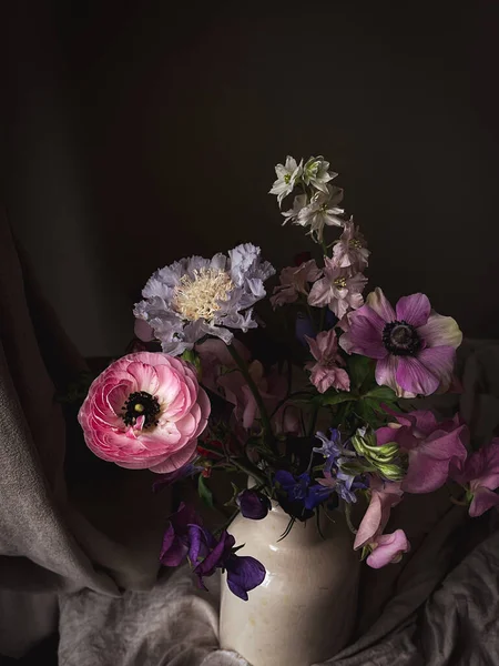 Beautiful flowers in vase on moody rustic background. Stylish flowers still life, artistic composition of lathyrus, anemone, ranunculus, delphinium. Floral vertical wallpaper