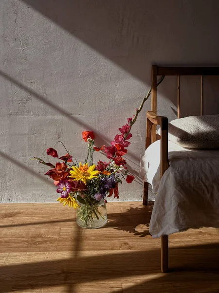 Beautiful flowers in vase in sunlight on background of modern retro chair and rural wall. Stylish flowers still life in home, artistic composition. Summer bouquet aesthetics